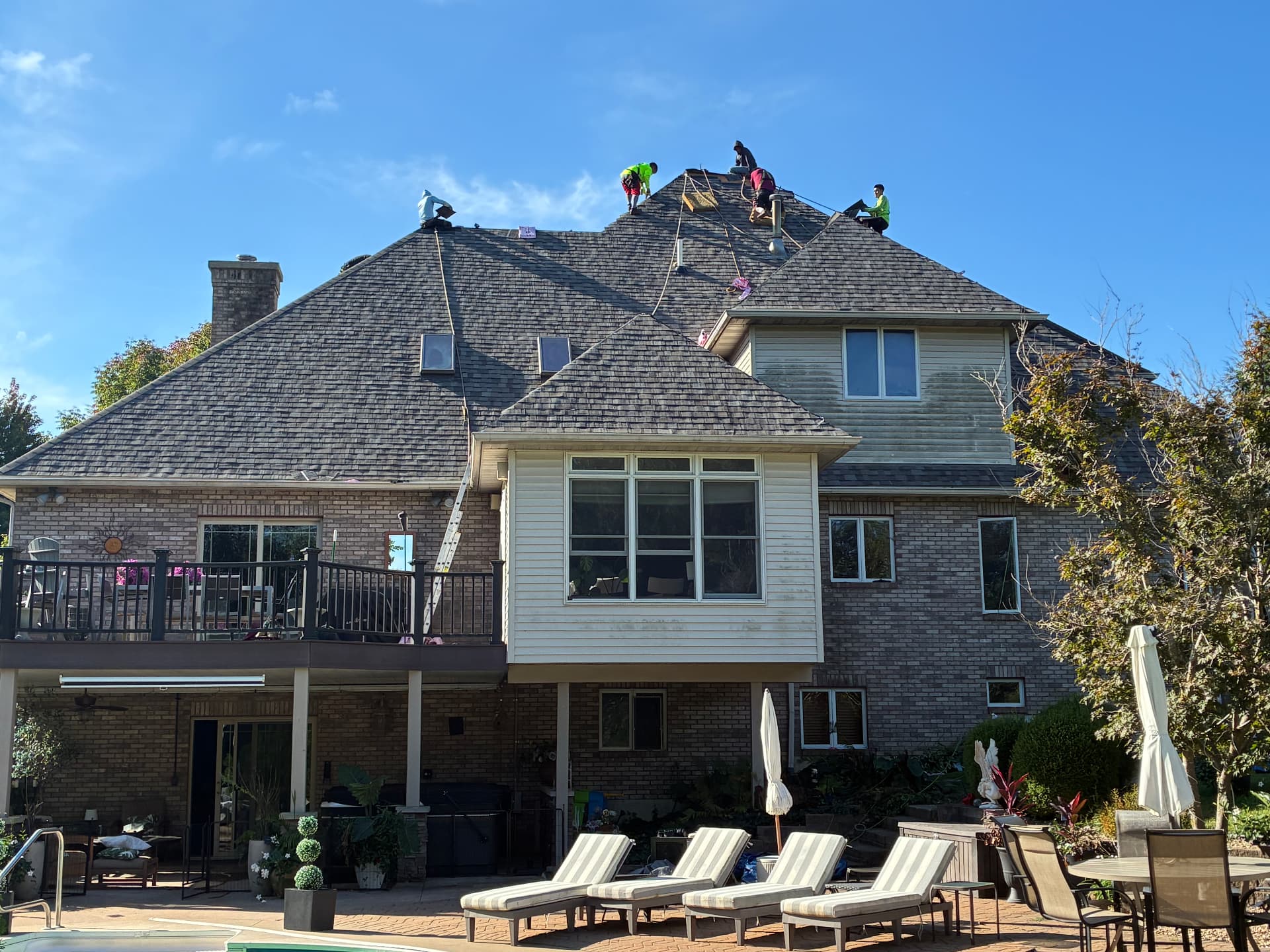 Milo's roofing crew installing shingles on the upper roof of a brick home