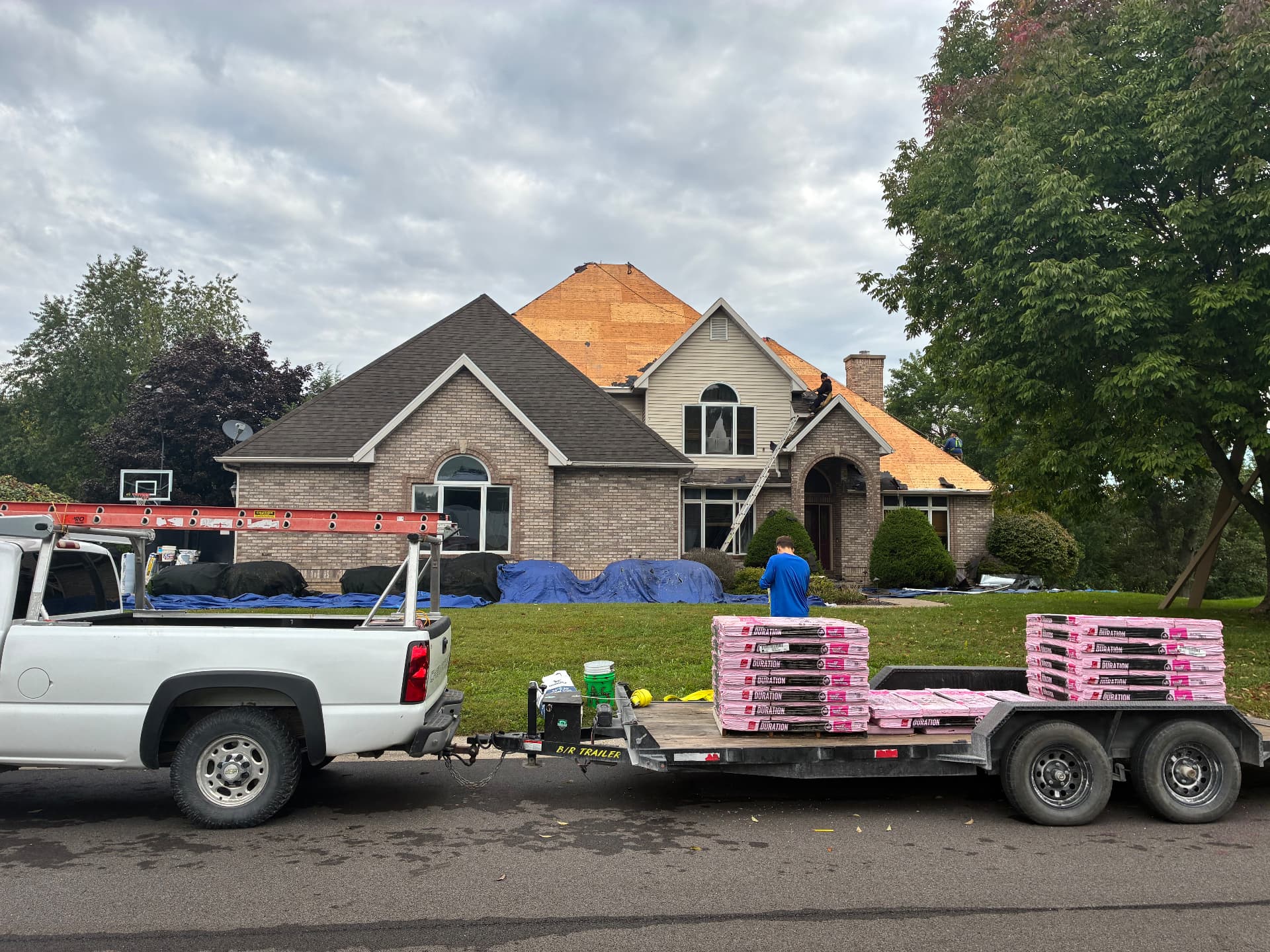 Shingle bundles on Milo's trailer in front of a brick home during roof replacement