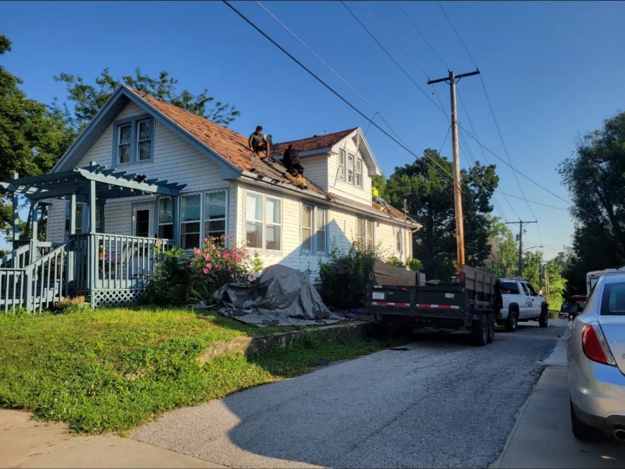 Tear-off of old shingles on a bungalow with dump trailer out front