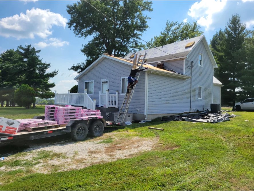 Roofer on a ladder during a tear-off with shingle bundles on the trailer