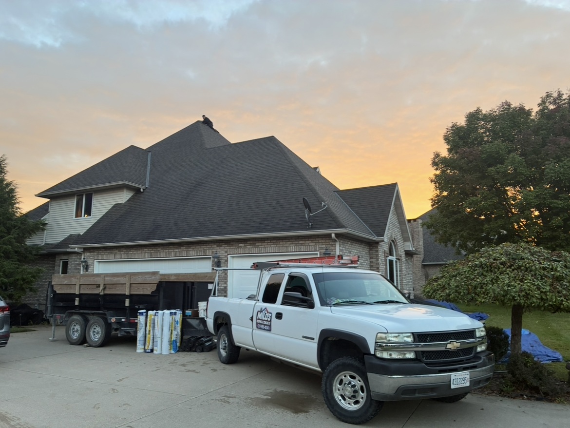 Milo's branded work truck and trailer parked in front of the roofing project at sunset